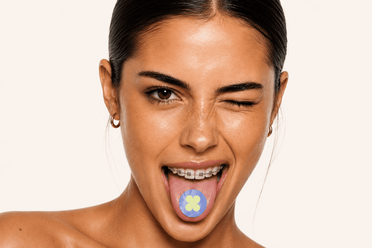 Modelo de campaña Xeito Dental guiñando un ojo, con brackets y una pegatina de flor sobre la lengua